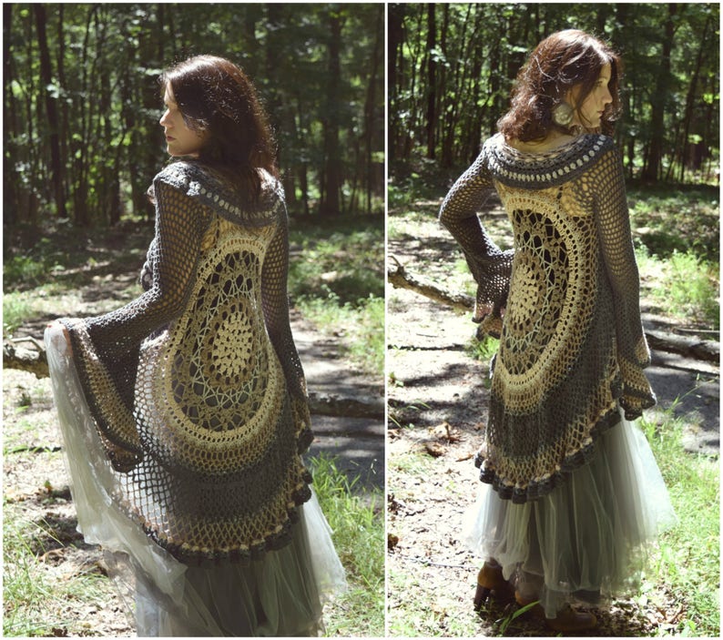 Pu&ograve; includere: Un lungo cardigan all'uncinetto con un grande disegno circolare sul retro. Il cardigan &egrave; grigio e beige con un orlo a scalare. La modella indossa il cardigan sopra una gonna di tulle in un ambiente boschivo.