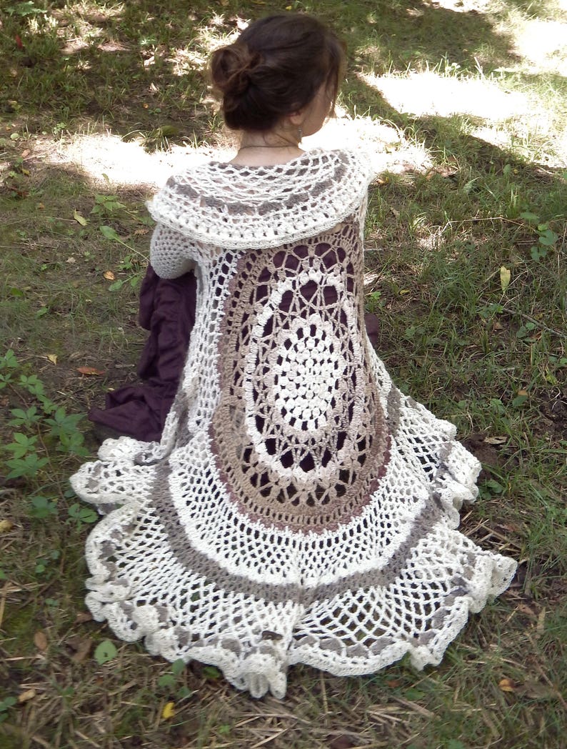 Pu&ograve; includere: Un cardigan bianco all'uncinetto con un design circolare marrone e bianco sul retro. Il cardigan ha un ampio colletto all'uncinetto e un orlo arricciato.