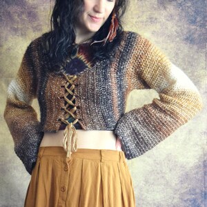 May include: A brown and white crocheted sweater with a lace-up front and long sleeves. The sweater is cropped and worn with a mustard yellow skirt.