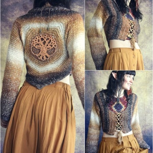 May include: A brown and white crocheted cropped sweater with a tree design on the back. The sweater has a lace-up detail in the front. The model is wearing a brown skirt.