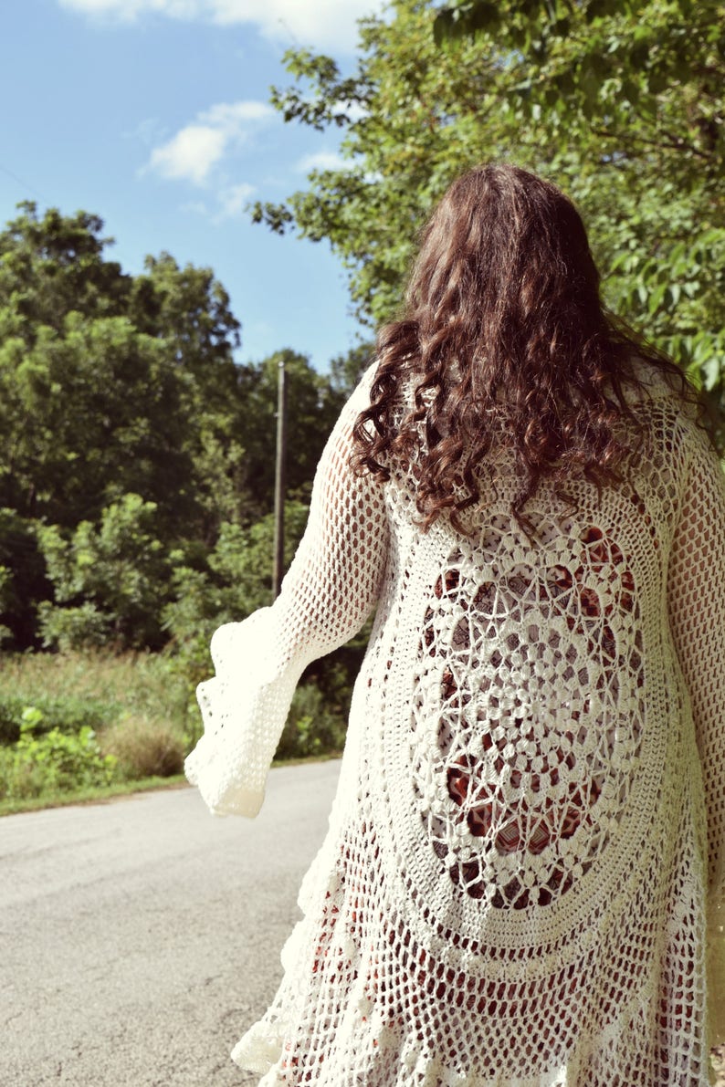 Pu&ograve; includere: Un cardigan bianco all'uncinetto con un grande disegno circolare all'uncinetto sul retro. Il cardigan ha maniche lunghe e un design fluido con apertura frontale.