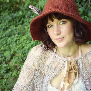 May include: A woman wearing a brown knitted pointed hat with a feather accent, a crocheted shawl, and a white dress with gold stars.