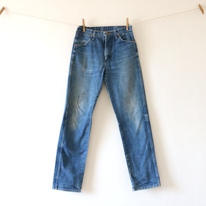 May include: A pair of blue denim jeans hanging on a clothesline. The jeans have a faded look and are slightly distressed.