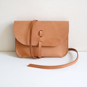 May include: A tan leather crossbody bag with a long strap and a flap closure. The bag has a simple design and is made of high-quality leather.