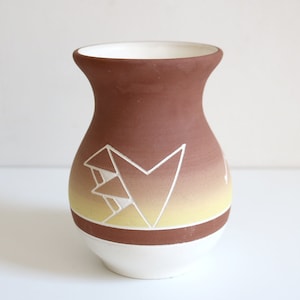 May include: A brown ceramic vase with a white geometric design and a yellow gradient. The vase has a wide mouth and a rounded base.