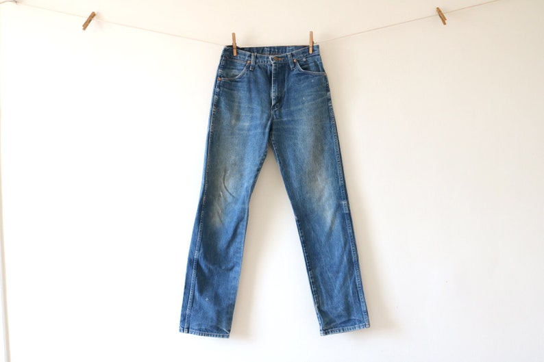 May include: A pair of blue denim jeans hanging on a clothesline. The jeans have a faded look and are slightly distressed.