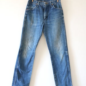 May include: A pair of blue denim jeans hanging on a clothesline with wooden clothespins. The jeans have a classic straight leg style and a light wash.