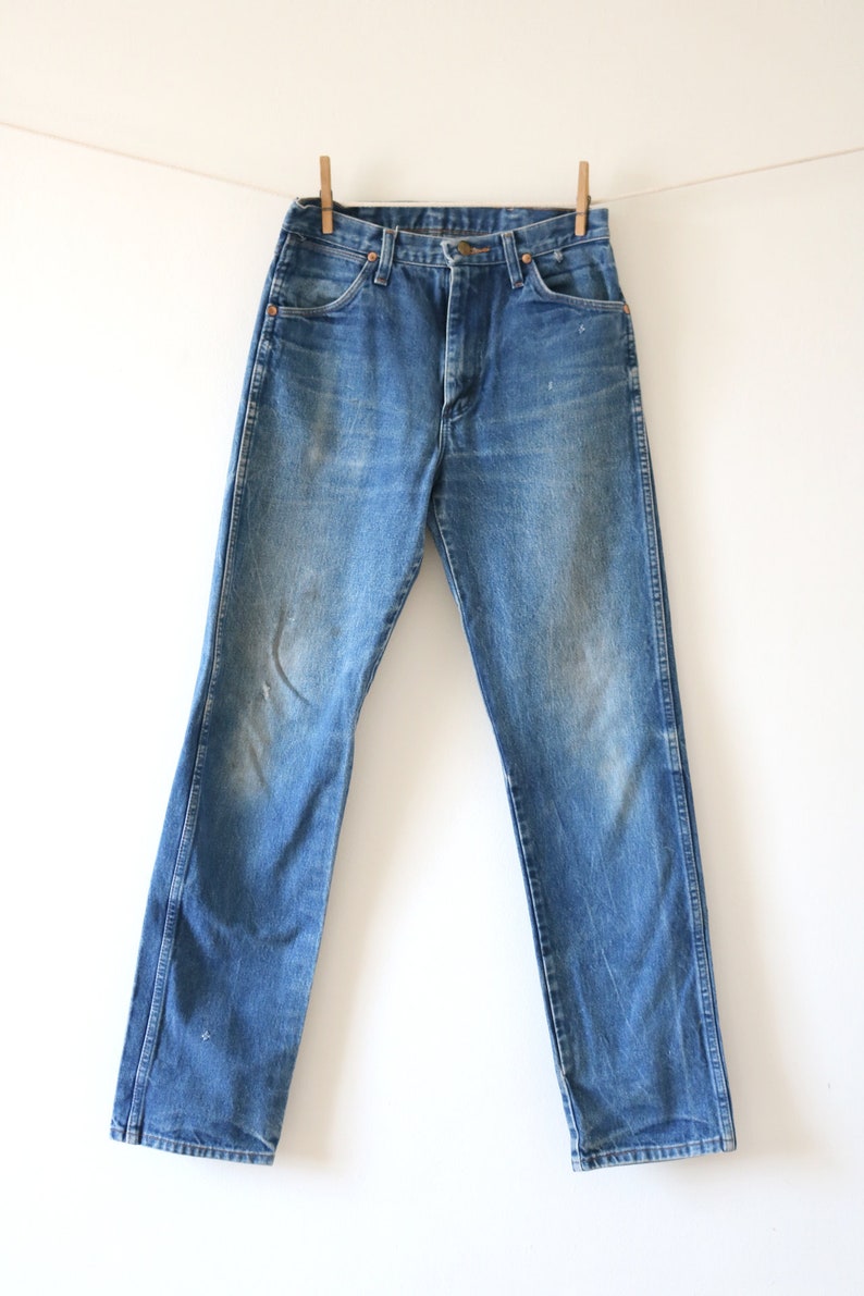 May include: A pair of blue denim jeans hanging on a clothesline with wooden clothespins. The jeans have a classic straight leg style and a light wash.