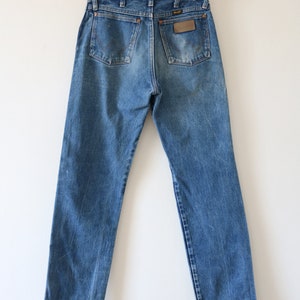May include: A pair of blue denim jeans with a brown leather patch on the back pocket that says "Wrangler".