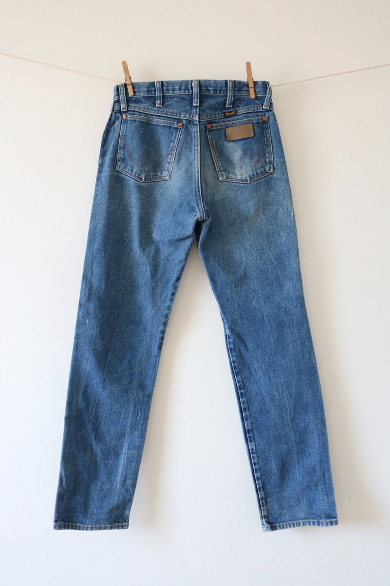 May include: A pair of blue denim jeans with a brown leather patch on the back pocket that says "Wrangler".