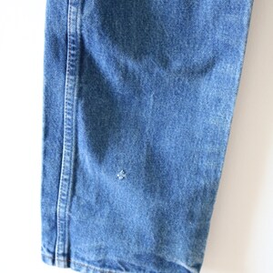 May include: Close-up of the bottom of a pair of blue denim jeans. The jeans have a single seam down the side and a small hole in the fabric.