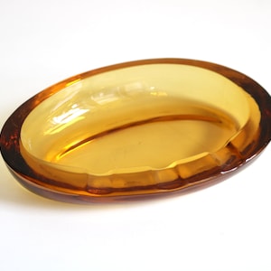 May include: An amber glass oval ashtray with a slightly raised rim.