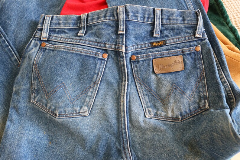 May include: A pair of blue denim jeans with a brown leather patch that says "Wrangler" on the back pocket.