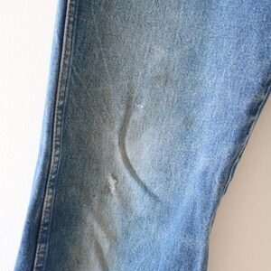 May include: Close-up of a pair of blue denim jeans with a small faded area on the knee.
