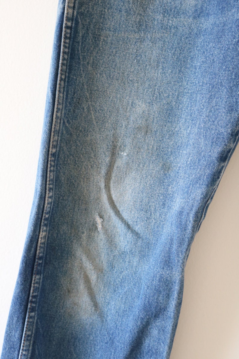 May include: Close-up of a pair of blue denim jeans with a small faded area on the knee.