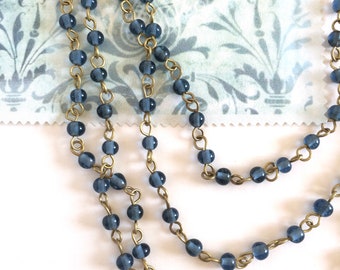 May include: A strand of dark blue glass beads strung on a brass chain. The beads are round and have a slightly frosted finish.