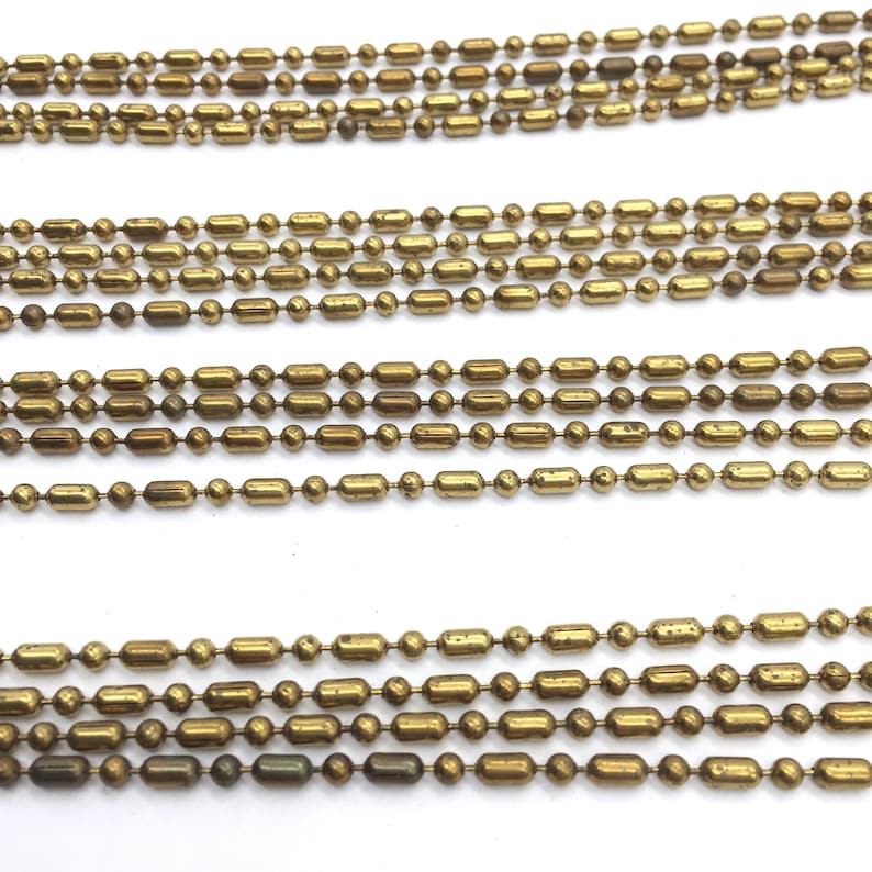 May include: Multiple strands of gold-toned metal chain with round and elongated links. The chain is laid out in parallel lines on a white surface.