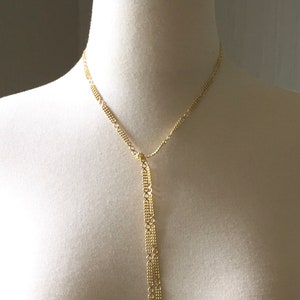 May include: A gold chain necklace with a long, dangling chain that is made of multiple strands of smaller chains.