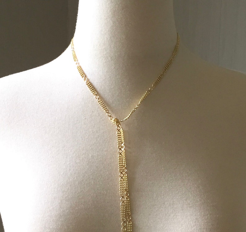 May include: A gold chain necklace with a long, dangling chain that is made of multiple strands of smaller chains.