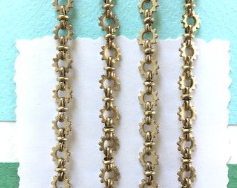 Könnte beinhalten: Drei goldene Ketten mit einem Zahnrad-Design. Jede Kette besteht aus kleinen, ineinandergreifenden Zahnrädern.