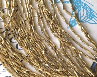 May include: A close-up of a pile of gold-colored chain links. The chain is made of small, twisted links that create a delicate and intricate pattern.