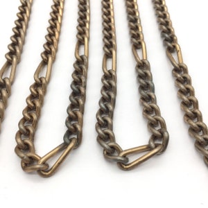 May include: Close-up of several antique silver-toned metal chains with alternating oval and rectangular links. The chains are arranged parallel against a white background, showcasing their texture and design. The chains are likely used for jewelry or accessories.