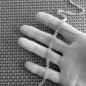 May include: A silver chain necklace with a delicate, linked design. The chain is lying on a hand, with the fingers spread out.