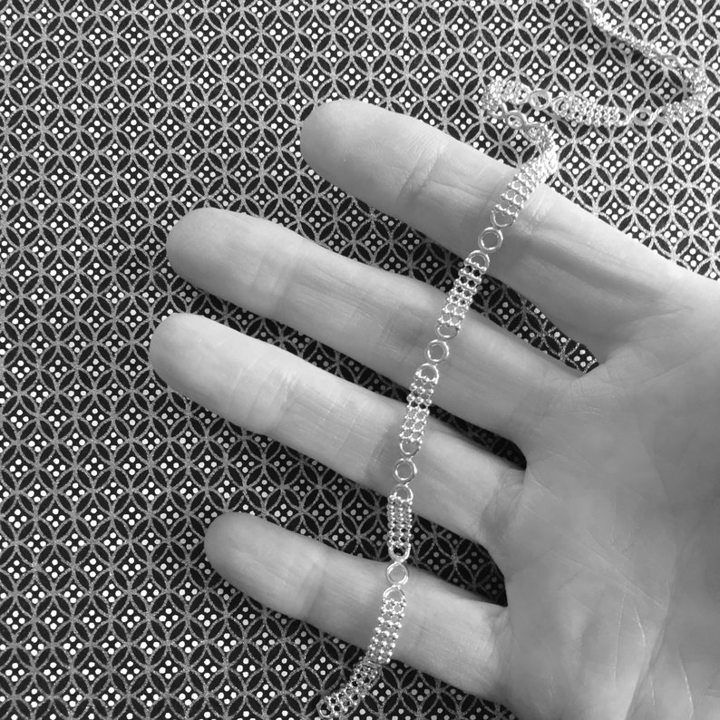 May include: A silver chain necklace with a delicate, linked design. The chain is lying on a hand, with the fingers spread out.