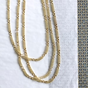 May include: Three gold chains with a textured, linked design. The chains are layered on top of each other and are photographed on a white surface.