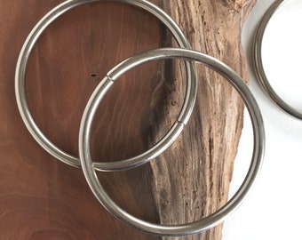 May include: Three silver metal rings of different sizes, lying on a piece of wood.