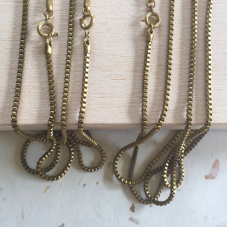 May include: Four gold-toned chain necklaces with lobster claw clasps. The chains are arranged in two pairs, with each pair overlapping.