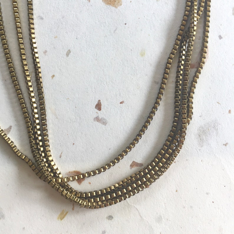 May include: A gold chain necklace with multiple strands of linked square-shaped metal.