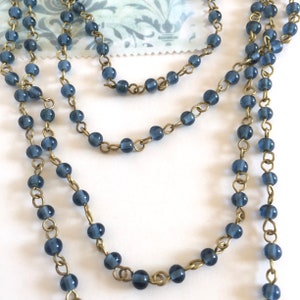 May include: A strand of blue glass beads strung on a brass chain. The beads are round and have a slightly frosted finish.