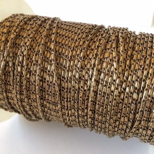 May include: A spool of gold-colored chain, tightly wound. The chain links are small and rectangular, creating a textured surface. The chain is likely used for jewelry making or other craft projects.