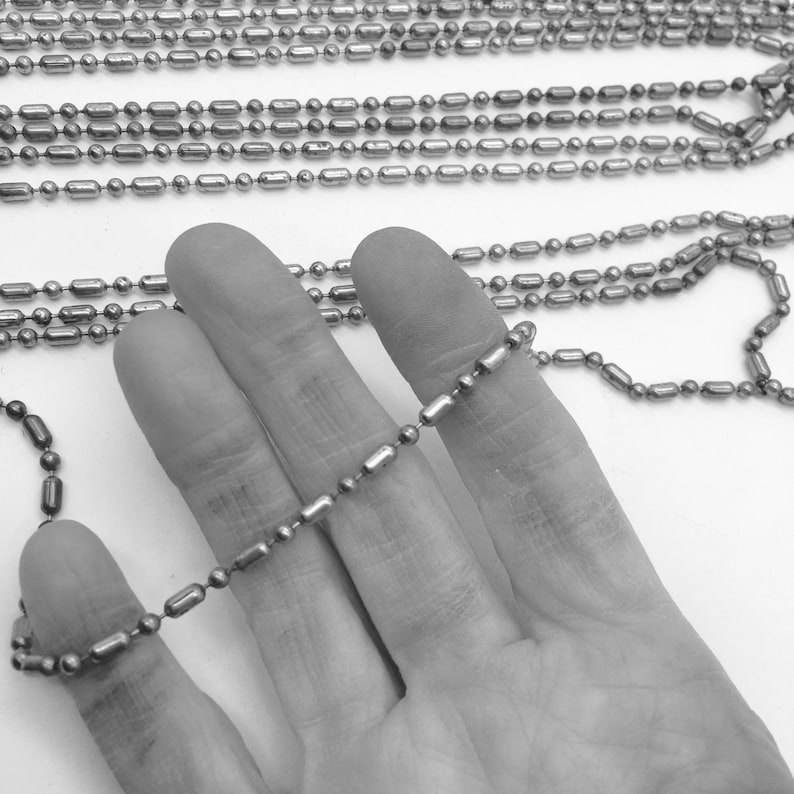 May include: A silver chain made of small, cylindrical links. The chain is held in a hand, showing the size and detail of the links.