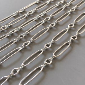 Könnte beinhalten: Nahaufnahme einer silbernen Kette mit ovalen Gliedern. Die Kette ist in Reihen ausgelegt und zeigt die verschiedenen Größen und Stile der Glieder.