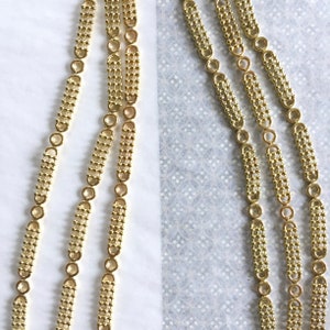 May include: Three strands of gold chain with a repeating pattern of small circles and rectangular links.