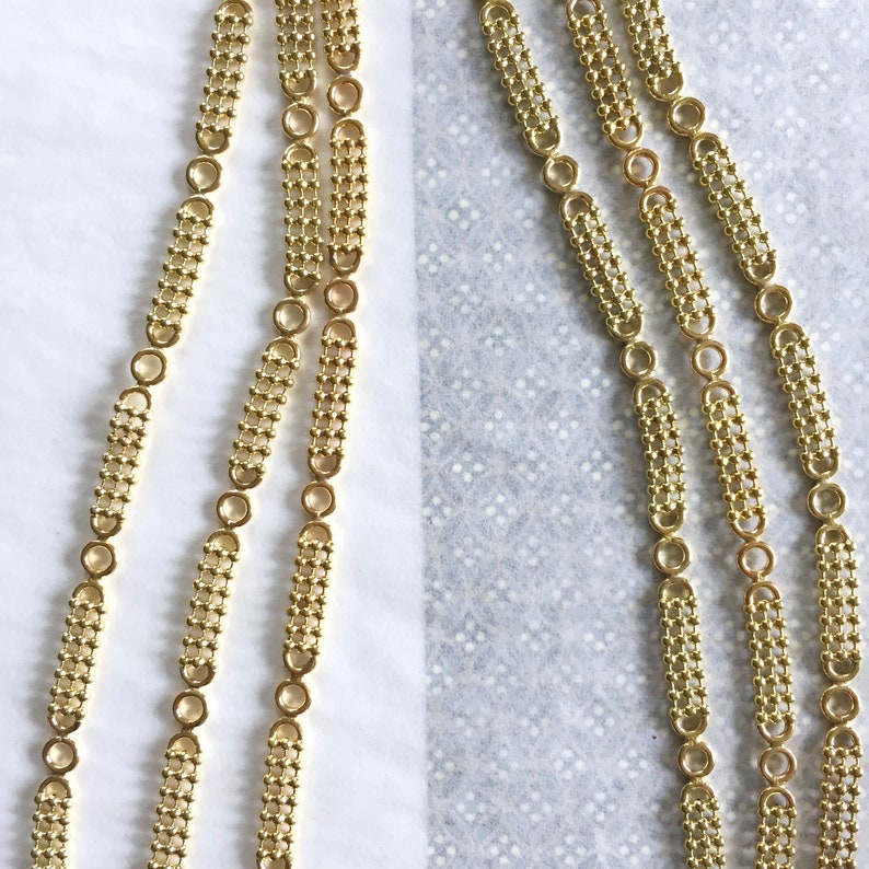 May include: Three strands of gold chain with a repeating pattern of small circles and rectangular links.