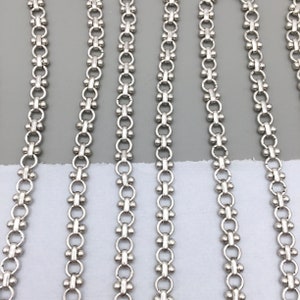 May include: Close-up of five strands of silver chain with a beaded design. The chains are laid out in parallel lines on a white surface.