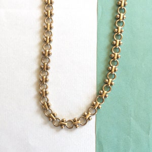 May include: A gold chain necklace with a delicate, linked design. The chain is made of small, round links that are connected together in a repeating pattern.