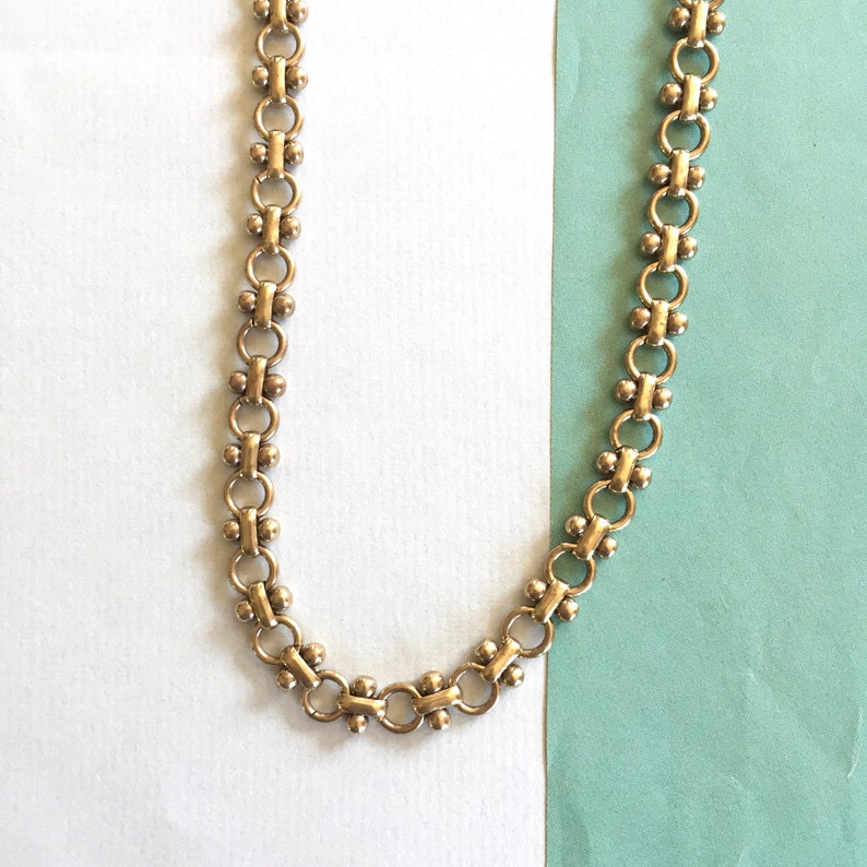 May include: A gold chain necklace with a delicate, linked design. The chain is made of small, round links that are connected together in a repeating pattern.