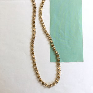 May include: A gold chain necklace with a delicate, linked design. The chain is made of small, round links that are connected together in a repeating pattern.