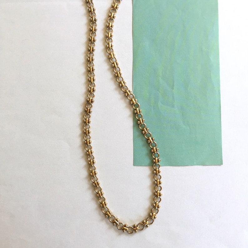 May include: A gold chain necklace with a delicate, linked design. The chain is made of small, round links that are connected together in a repeating pattern.