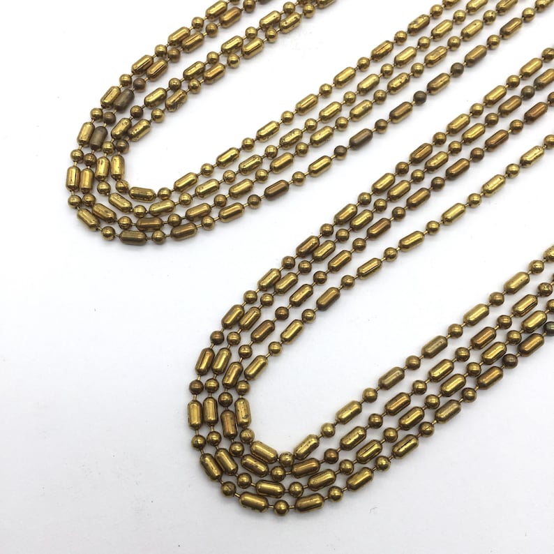 May include: A gold chain necklace made of multiple strands of small, round beads and elongated beads.