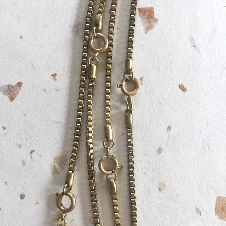 May include: Three gold chain necklaces with lobster claw clasps. The chains are layered on top of each other and are all the same length.