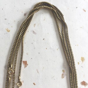 May include: A gold chain necklace with multiple strands. The chain is made of small, square links.