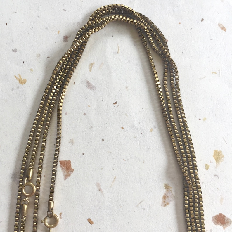 May include: A gold chain necklace with multiple strands. The chain is made of small, square links.
