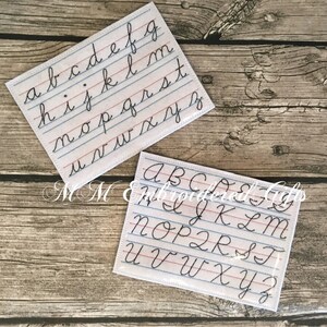May include: Two white rectangular patches embroidered with cursive alphabets. The patches feature blue and red ruled lines, mimicking notebook paper. One patch displays lowercase letters, the other uppercase. The text "MM Embroidered Gifts" is also visible.