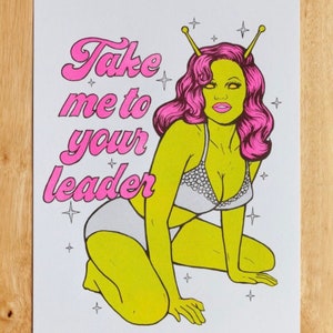 May include: A pink and green illustration of an alien woman with antennas, wearing a white bikini top and bottom. The text "Take me to your leader" is written in pink cursive letters.