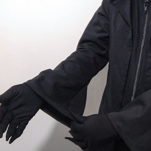 Könnte beinhalten: Eine schwarze Kapuzenjacke mit langen Ärmeln und Reißverschluss. Die Jacke hat einen hohen Kragen und ein langes, fließendes Design.